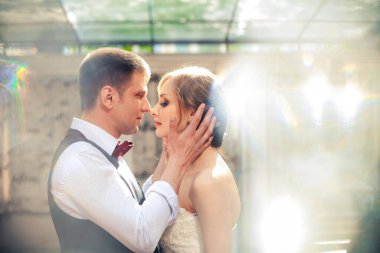 Sanat eserleri. Yeni evliler şık bir şekilde restoranın arka planına sarılıyorlar. Gelin hafif bir gelinlik giyiyor, damat beyaz gömlek, kazak ve papyon giyiyor..