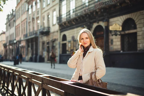 stock image A cute stylishly dressed girl with blond hair stands on the street of the old city, around beautiful buildings, on a bright sunny day.