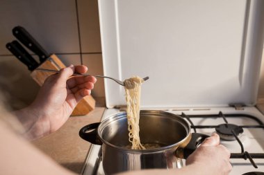 Sıcak hazır makarna mutfaktaki ocakta bir tencerede pişirilir. Kız çatalla kasedeki yemeği karıştırır. Yaratıcı dekorasyon ve tasarım için resim.