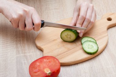 Tahta tahtada salata için sebze kesen bir kadın. Salatalık ve domatesler ahşap bir masada yatıyor. Sağlıklı gıda yaratıcılarınız için bir imaj..