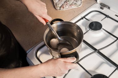 Bir kız mutfaktaki beyaz gaz sobasında metal bir tavada yumurta kaynatıyor. Yaratıcı dekorasyon veya tasarım için resim.