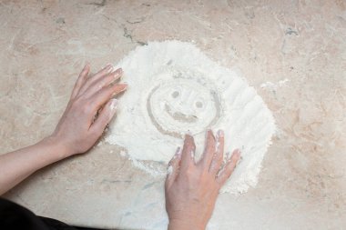 Kadın masadaki una parmaklarıyla gülen bir yüz çizdi. Yaratıcı tasarımın ya da dekorasyonun için canlı çekim.