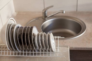 Mutfaktaki demir bir lavabonun arka planında, demir ızgarada büyük, beyaz cam ıslak tabaklar kurudu. Mutfak bakımı, daire temizliği, temizlik..