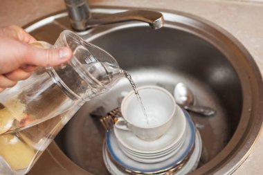 Elinde sürahi olan bir adam bulaşık, çatal, kaşık, tabak, bardak ve lavaboya su döker. Mutfak bakımı, daire temizliği, temizlik..