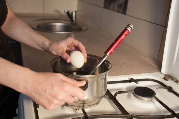 女の子は台所の白いガスストーブの上の金属鍋に卵を沸騰させます あなたの創造的な装飾やデザインの画像 — ストック写真