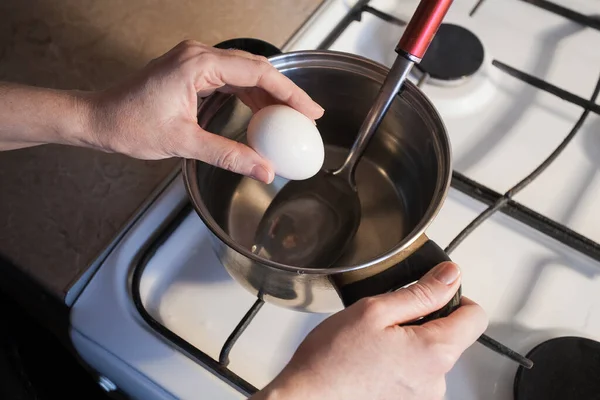 女の子は台所の白いガスストーブの上の金属鍋に卵を沸騰させます あなたの創造的な装飾やデザインの画像 — ストック写真