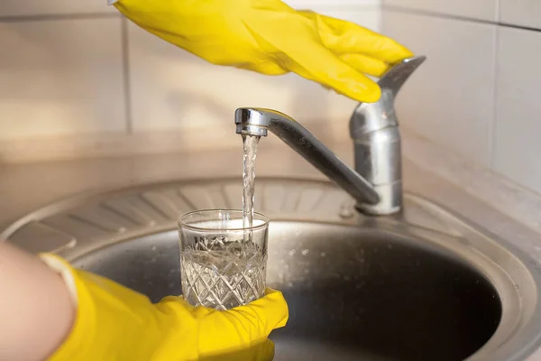 黄色のゴム手袋の少女は台所で水道水の下でガラスを洗う 清潔感 日々の活動をプロットします — ストック写真