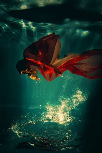 stock image Art work. Underwater shot of a sports girl with red material in the pool with beautiful highlights.