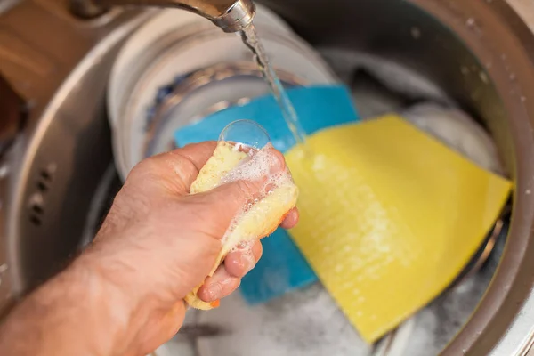 Washing dishes. A man\'s hand squeezes a soapy solution from a sponge, with a blue rag for washing dishes in the kitchen. An image about housework, apartment care and cleanliness.