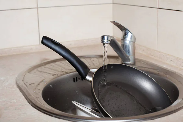 台所の水道水の下の洗面台には フライパンと大きな白いプレートが泡の中にあります キッチンケア アパートの掃除 — ストック写真