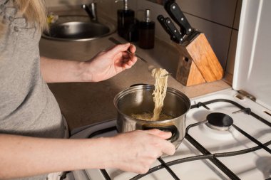 Sıcak hazır makarna mutfaktaki ocakta bir tencerede pişirilir. Kız çatalla kasedeki yemeği karıştırır. Yaratıcı dekorasyon ve tasarım için resim.