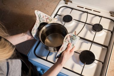 Kız mutfaktaki beyaz gaz sobasının üzerine metal bir tava koyuyor. Yaratıcı dekorasyon veya tasarım için resim.