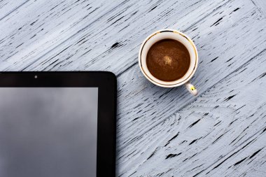 Bir bardak aromatik sade kahve ve açık ahşap bir masada siyah bir tablet..