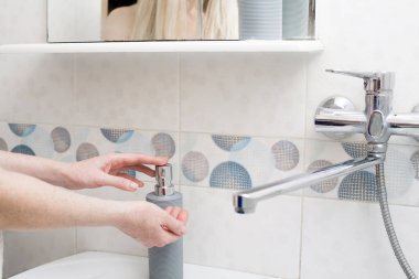 Banyodaki musluğun altındaki şişede sıvı sabunla ellerini yıkamak. Tasarımınız veya yaratıcı dekorasyonunuz için hijyen, kişisel bakım ve temizlik teması üzerine bir resim.