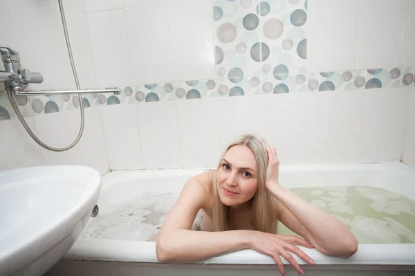 ブロンドの髪をした美しい笑顔の女の子がバスルームに座って 洗面所に座っています 清潔さと自分自身と自分の体の世話に関するイメージ — ストック写真