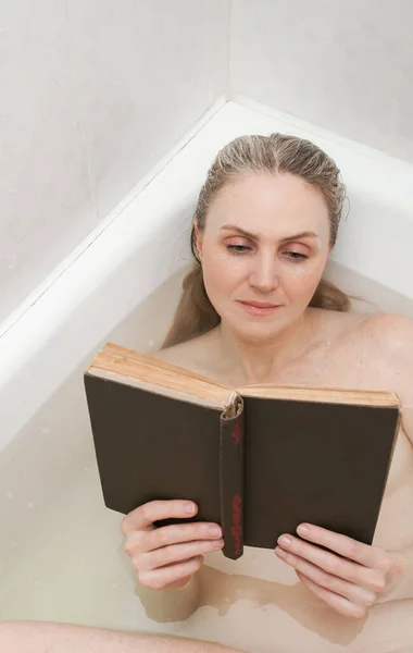 漂亮的金发姑娘躺在浴室的水底看书 休息一下 以照顾你的身体和家庭休闲为主题的图像 — 图库照片