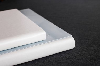 Deri kapaklı, farklı boyutlarda iki beyaz renkli fotobook bir odada koyu gri bir yüzeye uzanıyorlar. Tasarım ve yaratıcı çizimleriniz için bir arkaplan olarak bir resim.