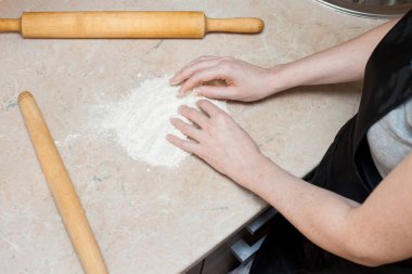 Bir kadın undan yiyecek hazırlar. Masanın üzerinde hamur yapmak için ahşap mutfak aletleri var. Bir kadının evdeki günlük yaşamının canlı görüntüsü..