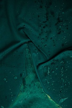 Droplets of water lie on a wet, crumpled green cloth. Dark creative image for your stylish design or illustrations.