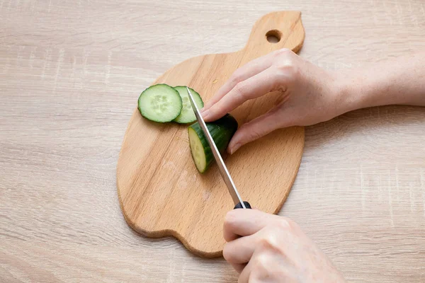 女性は板にサラダ用の野菜を切る キュウリは木製のテーブルの上にあります あなたの健康的な食品の創造者のための画像 — ストック写真