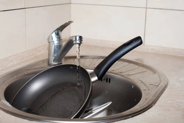台所の水道水の下の洗面台には フライパンと大きな白いプレートが泡の中にあります キッチンケア アパートの掃除 — ストック写真