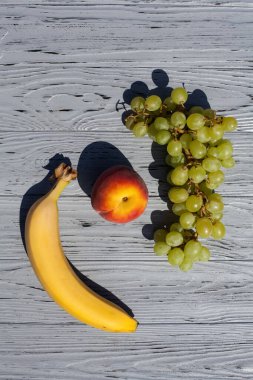 Tasarımınız veya çizimleriniz için açık ahşap bir masada olgun bir şeftali, muz ve bir demet üzümle dolu bir hayat..