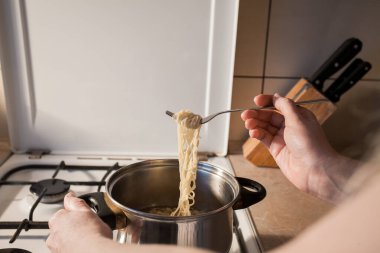 Sıcak hazır makarna mutfaktaki ocakta bir tencerede pişirilir. Kız çatalla kasedeki yemeği karıştırır. Yaratıcı dekorasyon ve tasarım için resim.