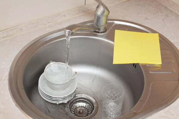 水のジェットが皿や洗面台のカップの上に流れ その横に黄色の洗面布があります キッチンケア アパートの掃除 — ストック写真