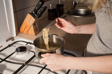 Sıcak hazır makarna mutfaktaki ocakta bir tencerede pişirilir. Kız çatalla kasedeki yemeği karıştırır. Yaratıcı dekorasyon ve tasarım için resim.