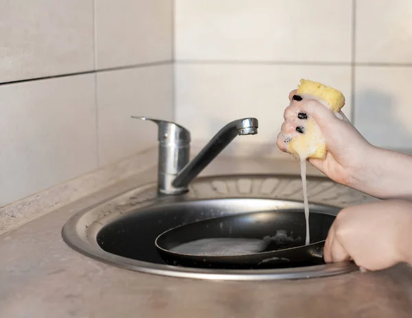 女の子は水道水の下でスポンジと石鹸で大きな汚れたフライパンを洗っています 台所の家事と清潔さをプロットします — ストック写真
