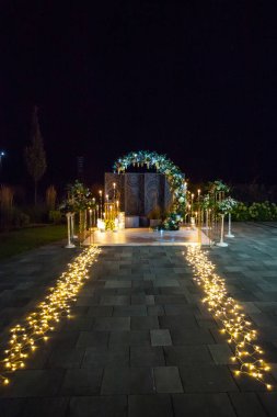 Şık bir düğün kemeri. Mumlar, fenerler ve taze çiçekler. Geceleri aydınlatılıyor. Tasarımınız veya çizimleriniz için yaratıcı resim.
