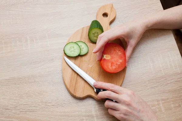 女性は板にサラダ用の野菜を切る キュウリとトマトは木製のテーブルの上にあります あなたの健康的な食品の創造者のための画像 — ストック写真
