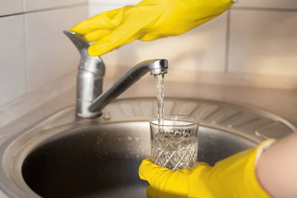 黄色のゴム手袋の少女は台所で水道水の下でガラスを洗う 清潔感 日々の活動をプロットします — ストック写真