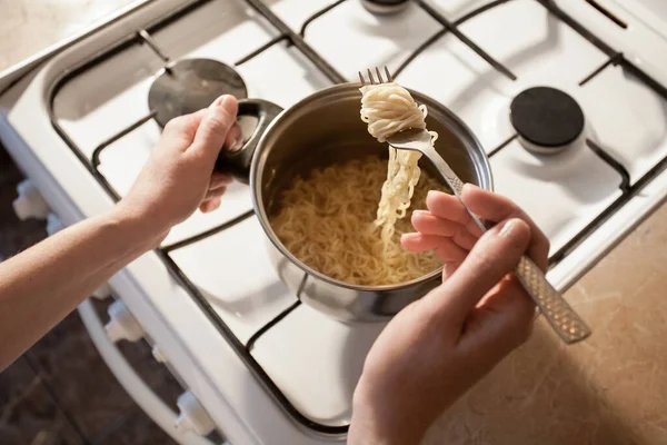 ホットインスタントパスタはキッチンのストーブの上の鍋で調理されます 女の子はフォークで鉢の中の食べ物をかきまぜる あなたの創造的な装飾とデザインのための画像 — ストック写真