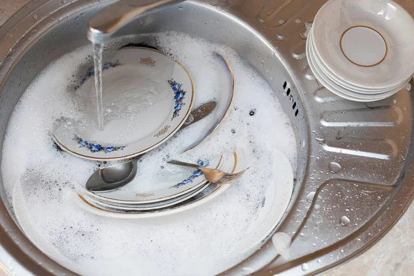 食器洗い フォーク スプーン 実行中の水の下でシンク内の異なるサイズのプレート 清潔感のイメージ — ストック写真