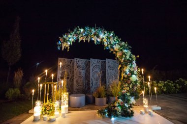 Şık bir düğün kemeri. Mumlar, fenerler ve taze çiçekler. Geceleri aydınlatılıyor. Tasarımınız veya çizimleriniz için yaratıcı resim.