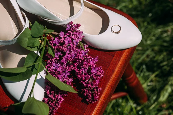 Romantic wedding arrangement of a pair of bride\'s shoes on a stool and wedding rings, in a blooming garden. Image for your creative design or illustrations.
