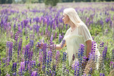 Açık renk iç çamaşırlı, kısa sarı saçlı, güzel hamile bir kız. Mor çiçeklerle dolu, pitoresk bir çayırda yürüyor ve dinleniyor..