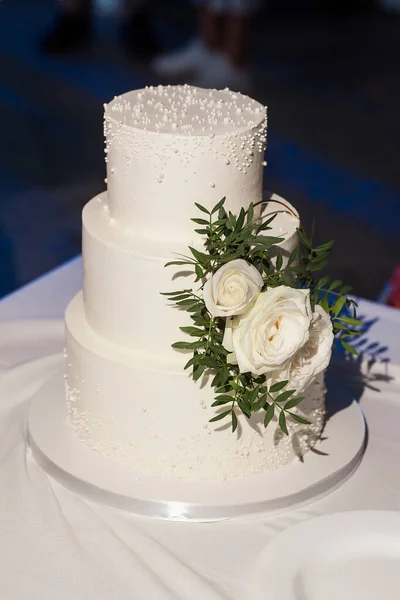 Stylish big white wedding cake decorated with white roses and fresh leaves. Image for your creative design or illustrations.