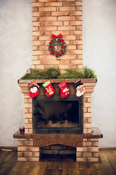 Home decorative fireplace made of bricks with candles, decorated with New Year's details, socks with toys, Christmas tree branches, Christmas wreath.