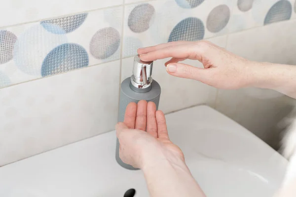 Washing hands with liquid soap in a bottle under the faucet in the bathroom. An image on the theme of hygiene, personal care and cleanliness for your design or creative decoration.