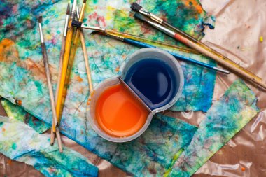 Sanatçının stüdyosundaki masanın üzerine soyut çizimler, fırçalar ve bir bardak su. Yaratıcı kaos. Tasarımlarınız ve web sayfalarınız için arkaplan.