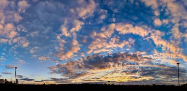 Cumulus gün batımı bulutları güneş batarken. Turuncu bulutların sihirli bukleleri akşam mavisi gökyüzünde muhteşem bir desen gibi diziliyordu. Sarı ve kırmızı yumuşak aksanlar, ılık ve soğuk tonlarda bir oyun.