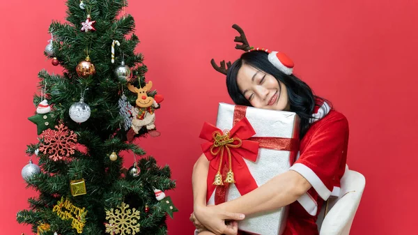 Happy young asia woman with red santy costume holding big gift box on red background.