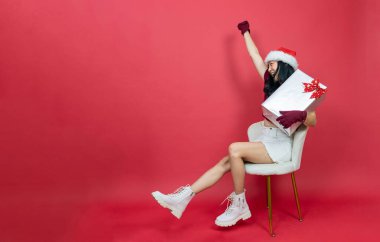 Noel Baba şapkalı güzel Asyalı kadının nezaketi büyük bir hediye kutusu tutuyor ve kazanan bir jest yapıyor. Başarı kutlaması.