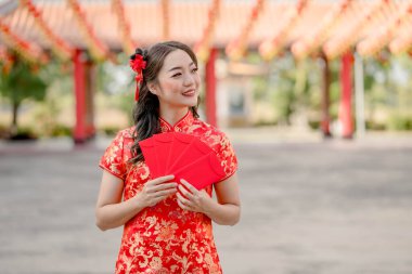 Beautiful Asian woman wearing traditional cheongsam qipao costume holding ang pao, red envelopes in Chinese Buddhist temple. Celebrate Chinese lunar new year, festive season holiday