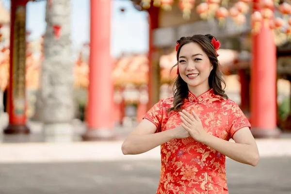 Happy Chinese new year. Beautiful Asian woman wearing traditional cheongsam qipao costume with gesture of congratulation in Chinese Buddhist temple.