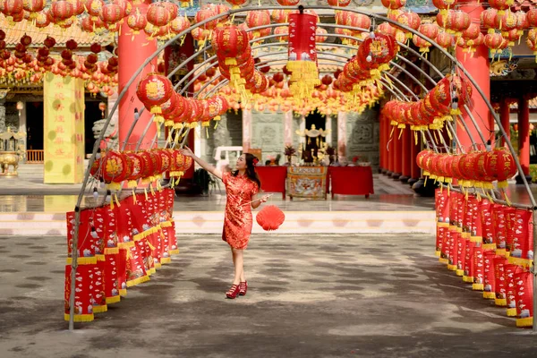 Beautiful young asian woman wearing traditional cheongsam qipao dress holding lantern and walk while visiting the Chinese Buddhist temple. Celebrate Chinese lunar new year, festive season holiday.