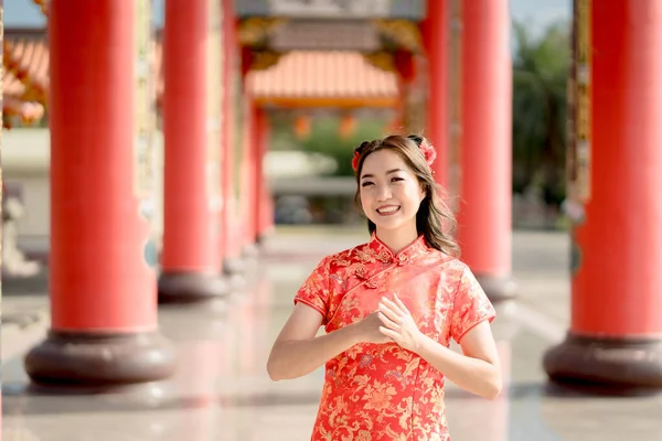 Asian woman wearing traditional cheongsam qipao dress with gesture of congratulation in Chinese Buddhist temple. Emotion smile. Chainese new year concept. Emotion Smile