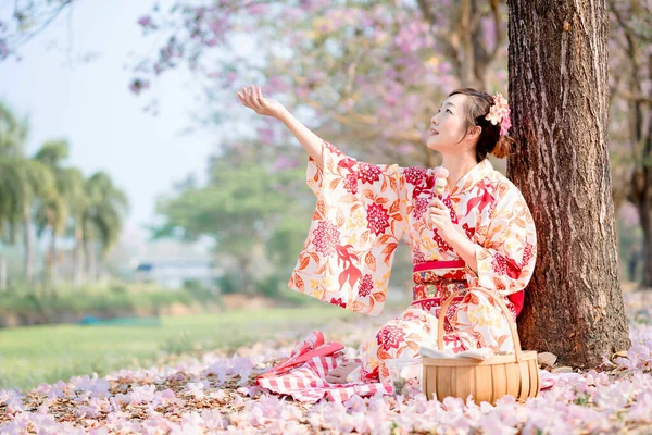 春祭りだ 伝統的な着物を着た若い女性が座って桜の木で団子を持っています — ストック写真